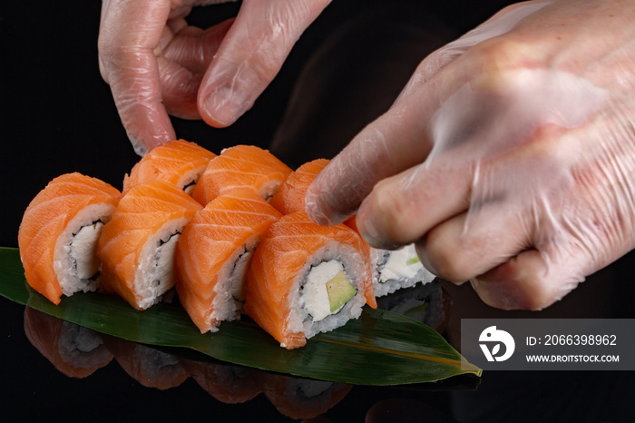 closeup of chef hands rolling up sushi - focus on the roll. Sushi with salmon, cheese and avocado