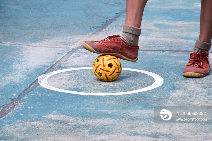 Young southeast asian male sepak takraw player using his right ankle to hold ball up on the serving center area of the court, outdoor sepak takraw playing after school, soft and selective focus.