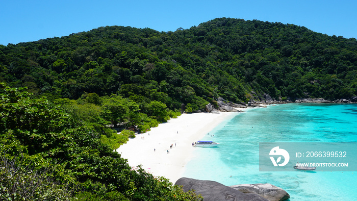 Turquoise water in the bay. View of the island and the sea. High cliffs covered with green trees. The gradient of water from blue to blue. There are speedboats, people swim in places. Similan Islands