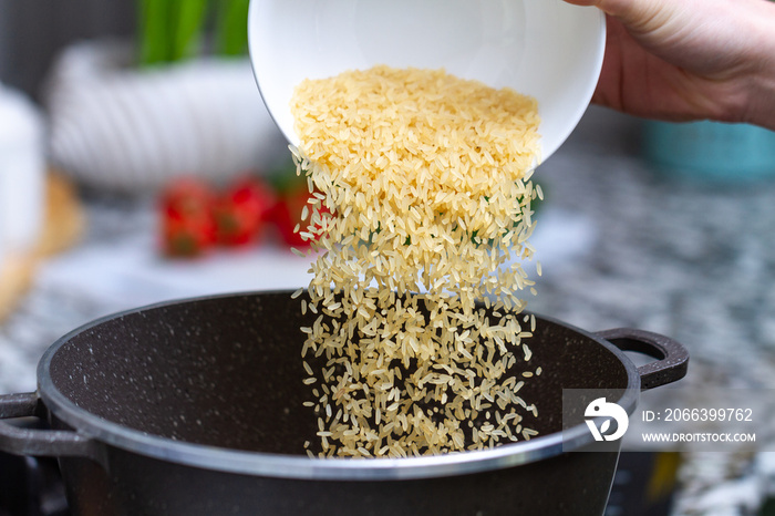 Cooking dry golden yellow long rice in a saucepan for delicious meals from groats with vegetables at home