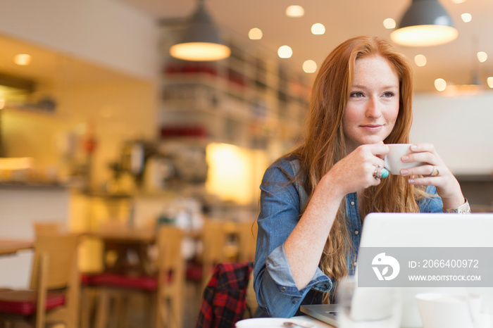 Smiling young woman drinking coffee and working at laptop in cafe