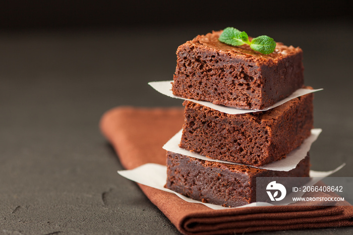 Chocolate brownie square pieces in stack on white plate with walnuts, decorated with mint leaves and