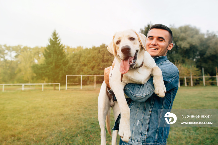 Portrait of happy man holding his friend dog labrador at sunset in park