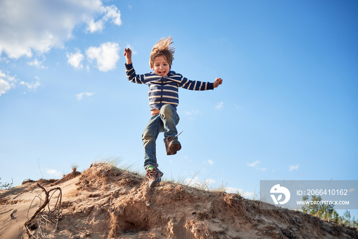 Happy boy jumping on sand at sunny day