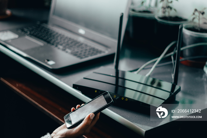 Wireless router and a young person using mobile phone with laptop on background at home – Multiple d