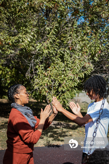 Black mother and teenager play hand games in park in fall