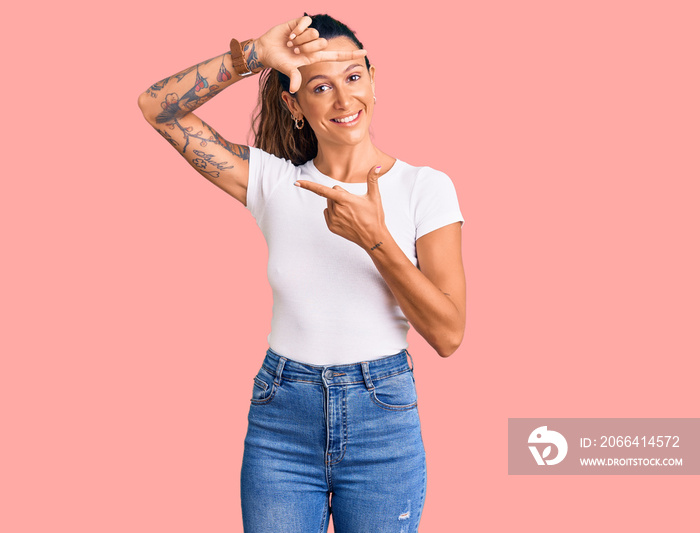 Young hispanic woman with tattoo wearing casual white tshirt smiling making frame with hands and fin