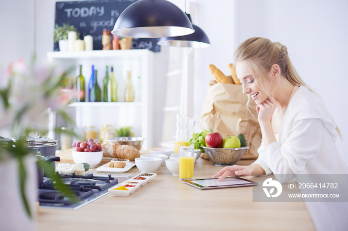 Beautiful young woman using a digital tablet in the kitchen