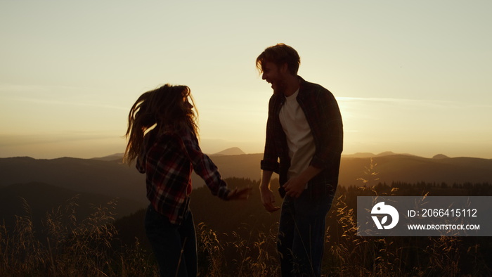 Smiling woman and man dancing together on top of mountain at sunset