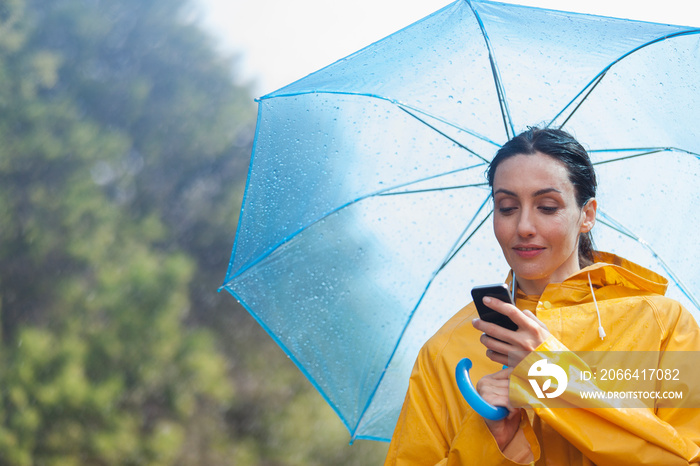 Woman with umbrella using smart phone in rain