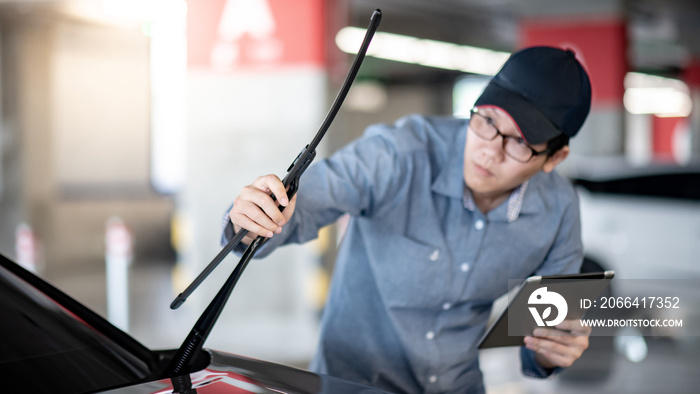 Young Asian auto mechanic holding digital tablet checking windshield wiper in auto service garage. M