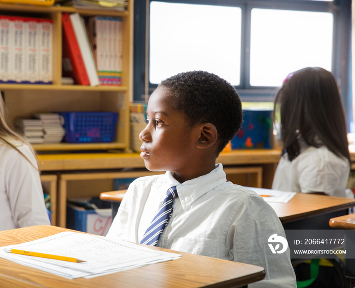 Thoughtful school boy sitting at desk in classroom