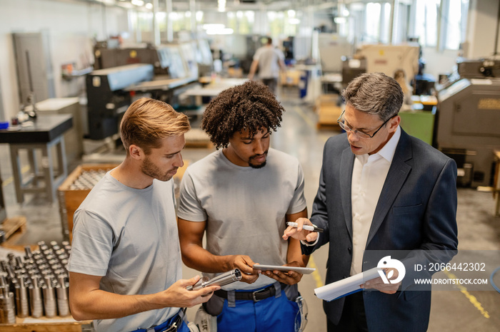 Engineer and two metal workers cooperating while using touchpad in industrial building.