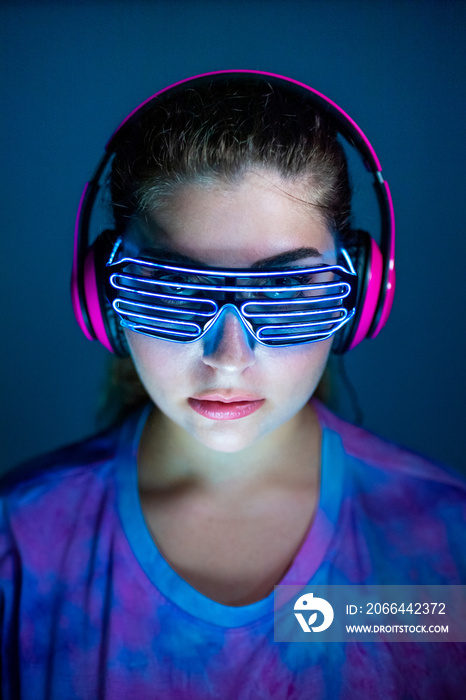 戴着耳机和蓝色背景未来主义led眼镜的年轻女性——与世隔绝的女性俱乐部