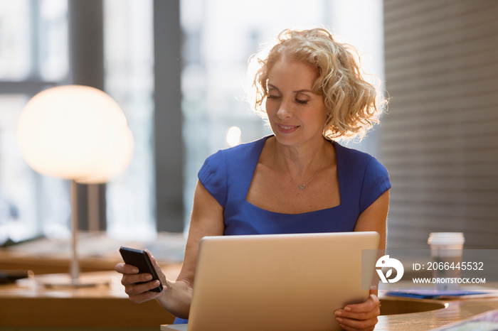 Corporate businesswoman using smart phone at laptop