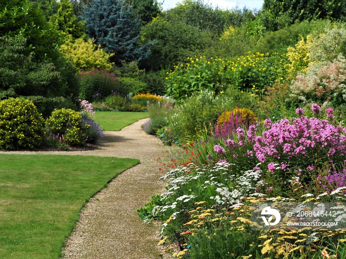 English garden with a grass lawns, summer flower borders, and background treesgarden paths and