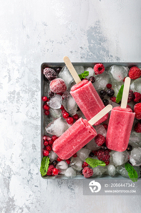 Homemade strawberry popsicles on metal plate with ice, assorted berries and mint. Healthy summer foo