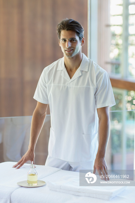 Portrait confident male masseuse standing at spa massage table