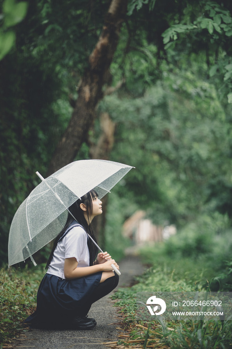 Portrait of Asian school girl sitting with umbrella at nature walkway on raining