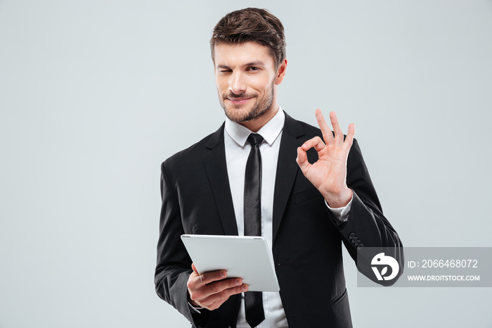 Happy young businessman with tablet winking and showing ok sign