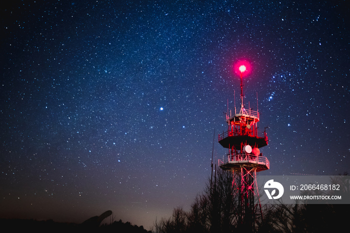 在美丽的星夜下，红色的天线塔被红光照亮。通讯器上方的壮丽天空