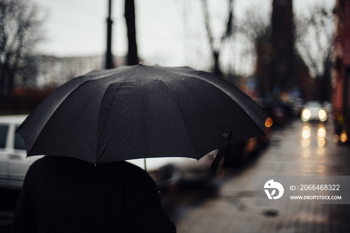 拿着一把闪闪发光的雨伞走在背景模糊的街道上