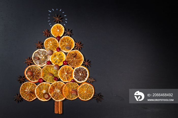 Christmas tree made of dried oranges, cinnamon and star anise on dark background. Viewed from above.