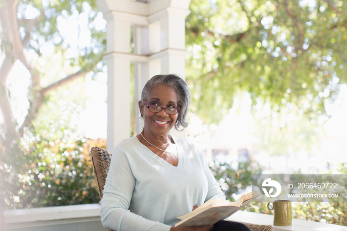 Portrait happy senior woman reading book on sunny porch