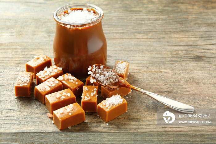 Tasty salted caramel in jar with candies on wooden table