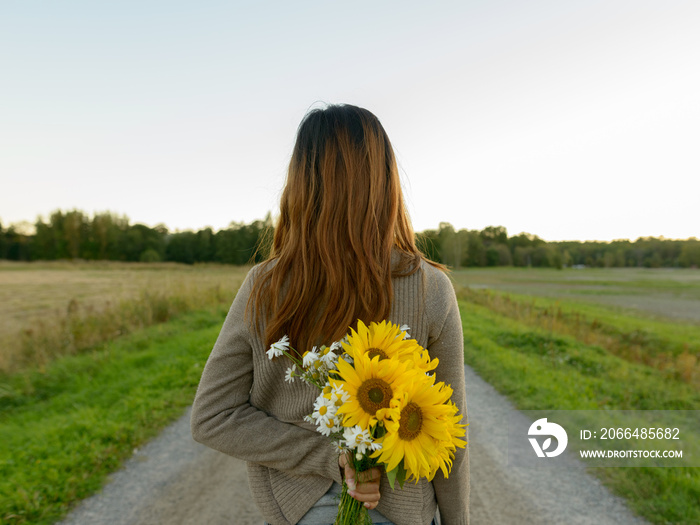 Rear view of young Asian woman holding sunflowers behind back in nature