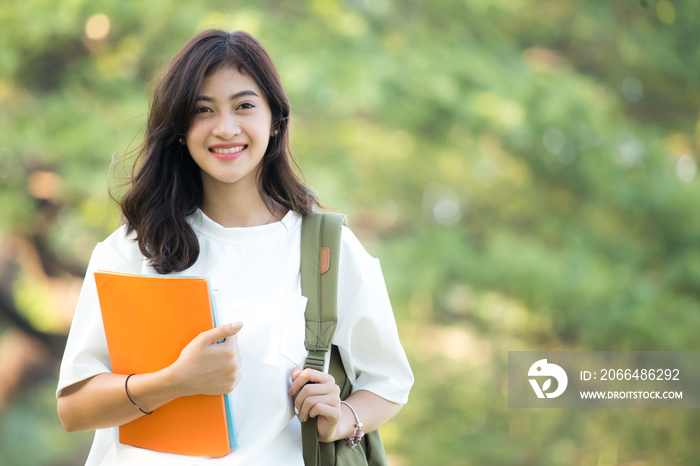 亚洲女人在公园里拿着书，面带迷人的微笑。有教育观念的女人。