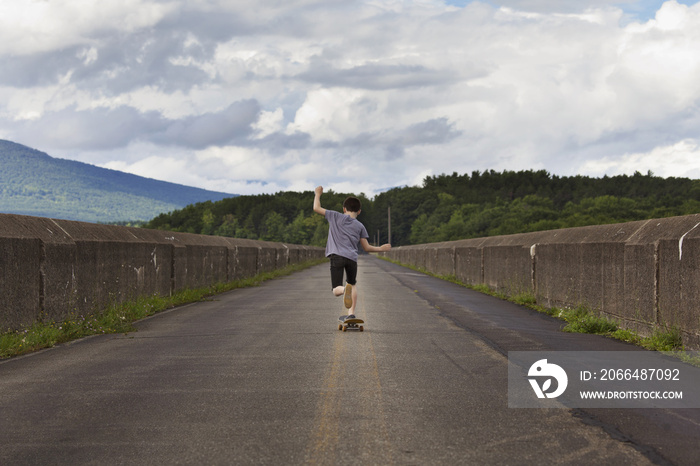 男孩在挡土墙旁的道路上玩滑板的后视图