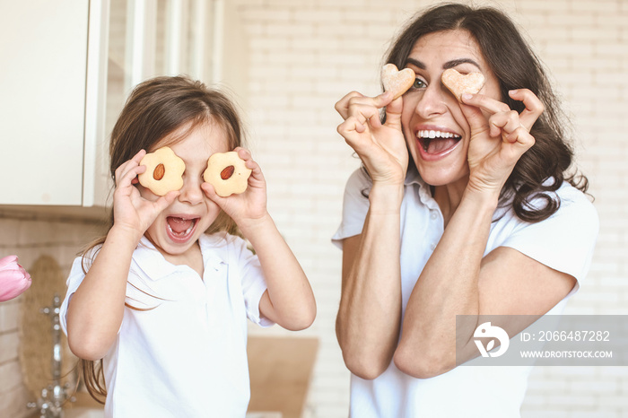 Happy mother and daughter with tasty cookies having fun in kitchen at home