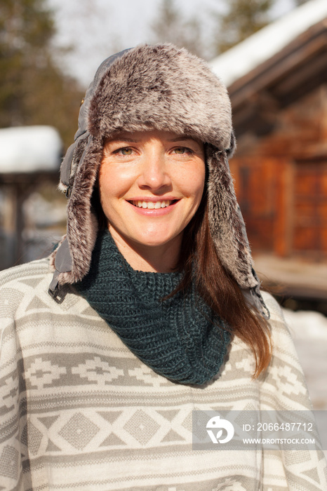 Portrait smiling woman in fur hat outside sunny cabin