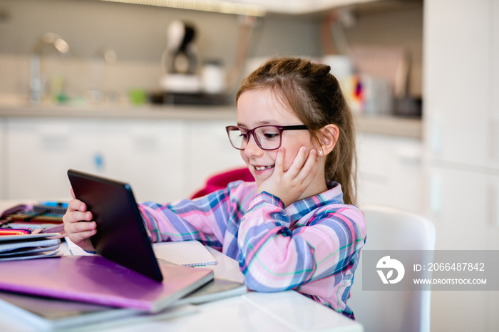 Cute little girl holding tablet while doing her homework.