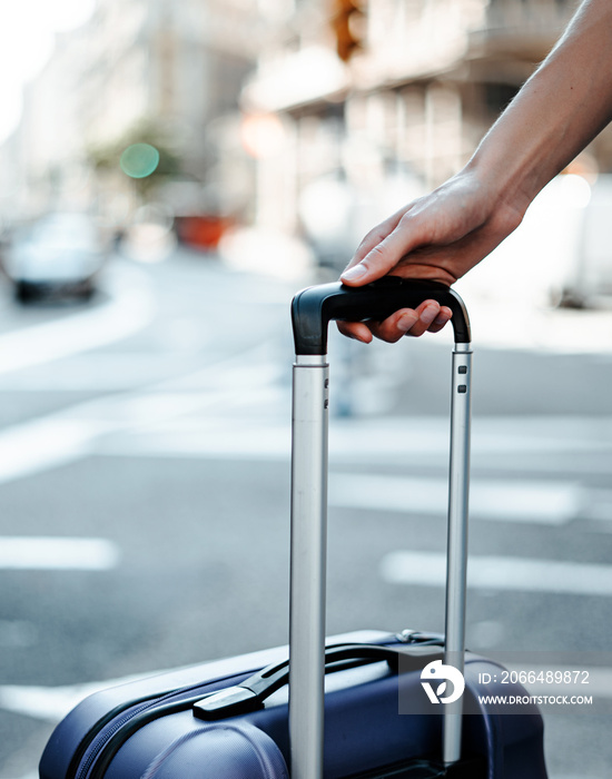 Close-up of a female hand holding suitcase. Young traveling woman with luggage on a city street. Tra