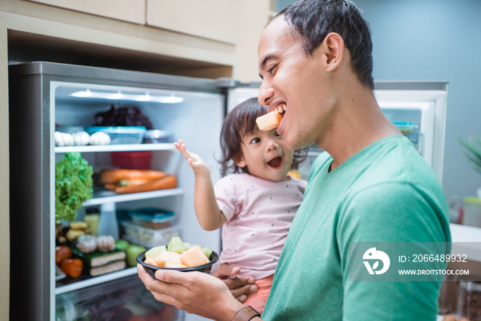 asian father and daughter open refrigerator at home having some fresh fruit together