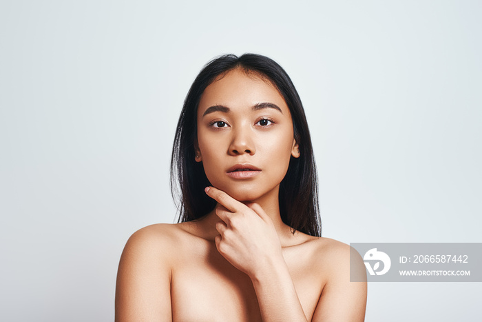 Perfect skin. Portrait of beautiful asian woman touching her skin and looking at camera while standi