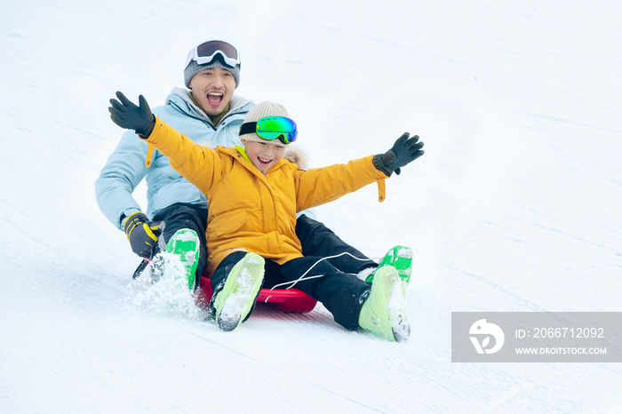 快乐父子坐着雪上滑板滑雪