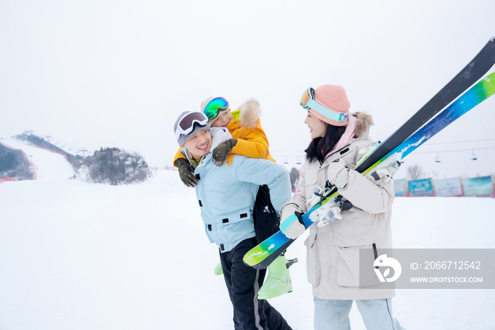 滑雪场上背着儿子的父亲和抱着滑雪板的母亲