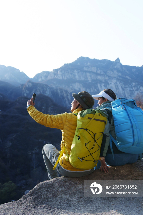 青年登山者伴侣坐在岩石上自拍