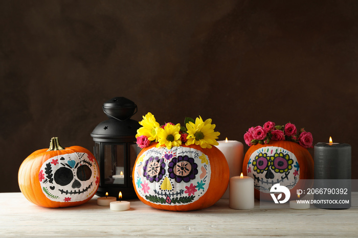 Pumpkins with catrina skull makeup and halloween accessories on brown background