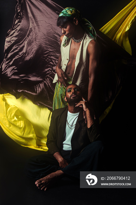 Two Malaysian Indian men in a studio setting with cloth flying in the background, posing against a b