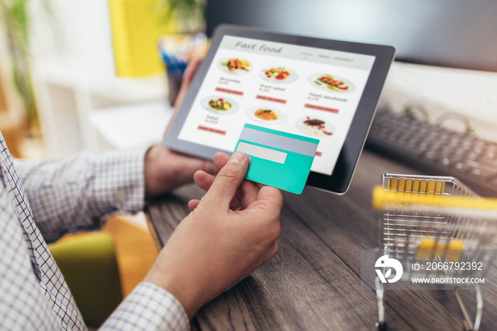 Hands of a man ordering fast food with a digital tablet, paying with credit card.