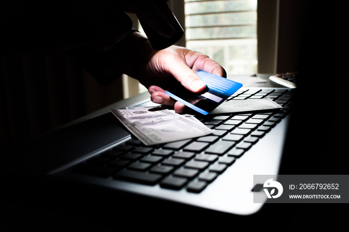 Hands of anonymous hackers shining a flashlight for using credit card on keyboard of laptop for remo