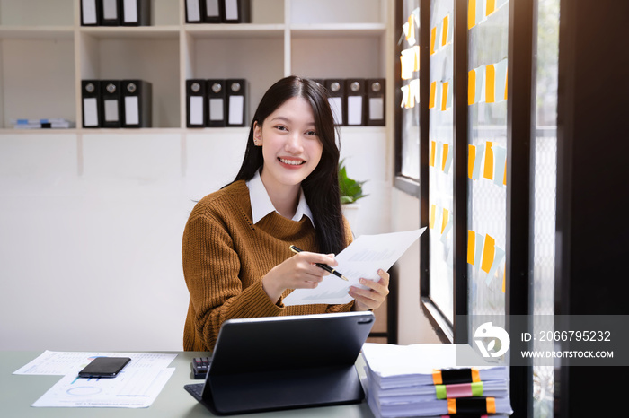 Smiling young asian woman succeeding in business using laptop and computer while doing some paperwor