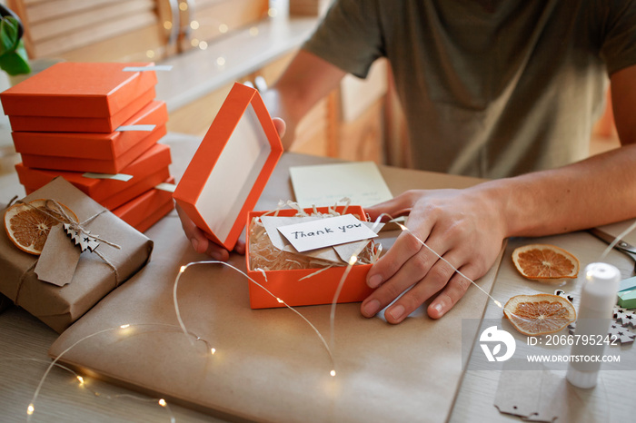 Hands of young millennial worker packing Christmas gift boxes for clients, family small business. Ne