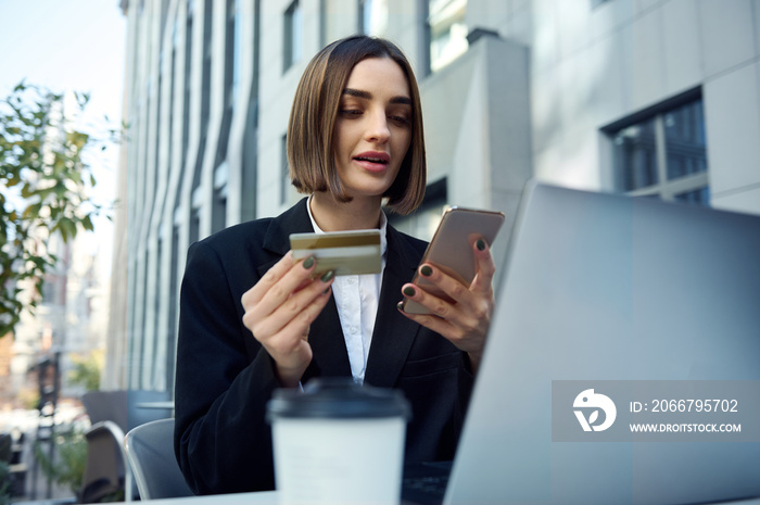 Pretty woman, entrepreneur, copywriter holding mobile phone and gold credit card sitting at table in