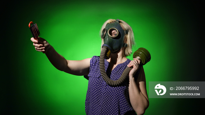 a woman in a gas mask with a comb in her hands, points the direction to the side on a dark backgroun