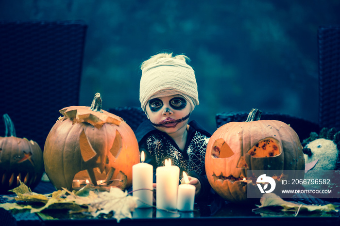 Scary toddler child in halloween costume, playing with carved pumpkins